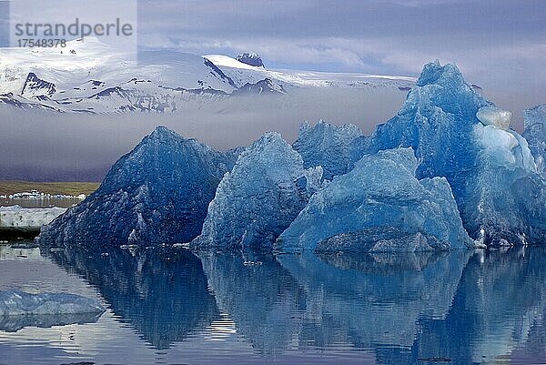 Blauer Eisberg spiegelt sich im ruhigen Wasser  Berge ragen aus dem Nebel  Jökulsarlon  Gletscherlagune  Skandinavien  Island  Europa