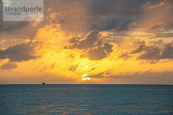 Dramatischer Himmel bei Sonnenuntergang über dem Meer mit Fischerboot in der Ferne