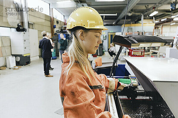 Seitenansicht einer Arbeiterin mit Schutzhelm  die in einer Fabrik Maschinen bedient