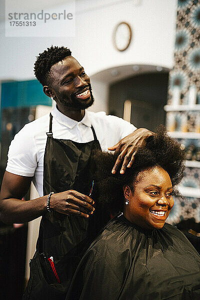 Lächelnder männlicher Friseur  der einer Kundin im Salon die Haare schneidet