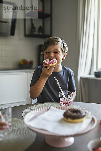 Junge isst Doughnut am Wohnzimmertisch