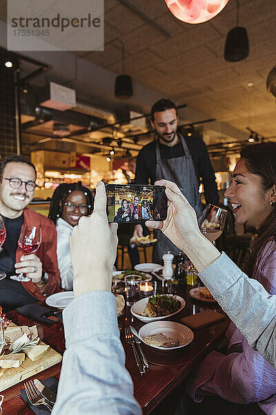 Ausgeschnittenes Bild eines Mannes  der mit seinem Handy in einer Bar ein Foto von einem Mann und einer Frau macht