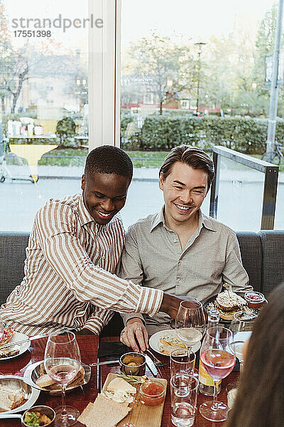 Lächelnde Männer beim Essen mit einem Freund am Tisch im Restaurant