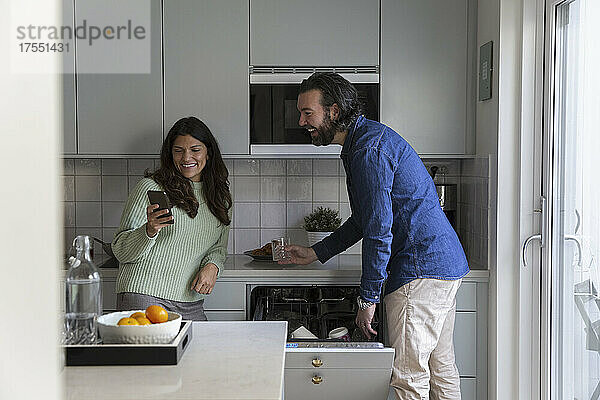 Lächelnde Frau teilt Smartphone mit Mann in Küche