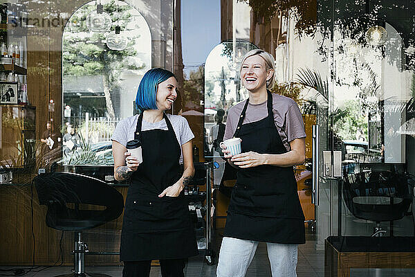 Fröhliche Mitarbeiterin mit Kaffeetasse  die vor einem Friseursalon steht