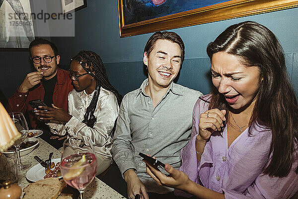 Glückliche Frauen  die ihr Smartphone benutzen  während sie mit ihren männlichen Freunden im Restaurant auf einer Party sitzen