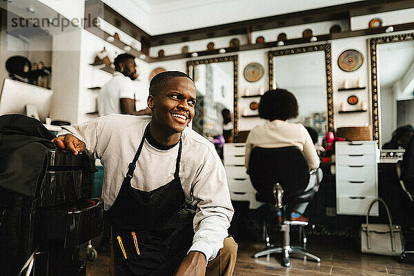 Lächelnder männlicher Friseur  der im Friseursalon wegschaut