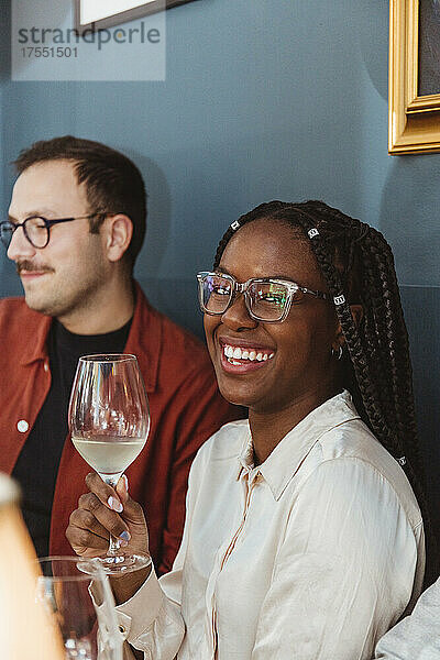 Porträt einer glücklichen Frau mit Wein  die neben einem männlichen Freund im Restaurant sitzt