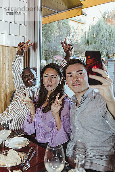 Männliche und weibliche Freunde machen ein Friedenszeichen  während sie ein Selfie mit ihrem Smartphone in einer Bar machen