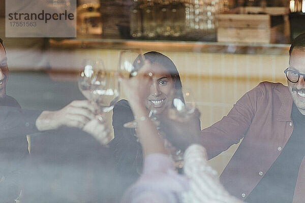 Männliche und weibliche Freunde stoßen mit Weingläsern an  gesehen durch das Glas einer Bar