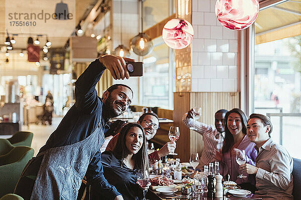 Glücklicher Kellner  der ein Selfie mit einem Kunden im Restaurant auf seinem Smartphone macht