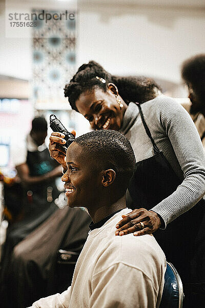 Lächelnde Friseurin schneidet einem männlichen Kunden die Haare mit einem elektrischen Rasiermesser im Salon