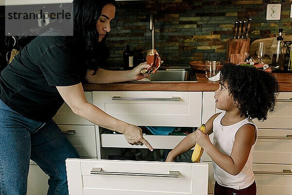 Mutter zeigt auf Tochter  die ihre Hand in eine Schublade in der Küche steckt