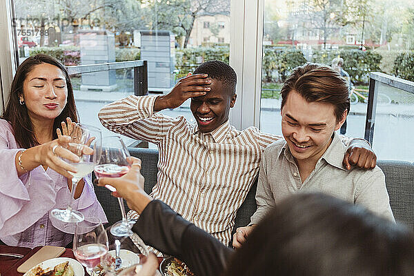 Glückliche Frauen stoßen mit Weingläsern an  die von männlichen Freunden in einer Bar während einer Party gehalten werden