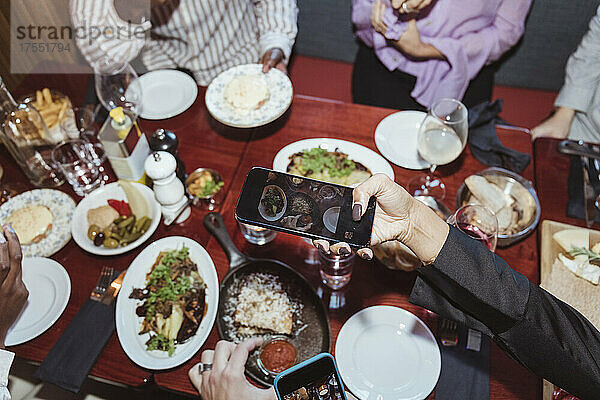Ausgeschnittenes Bild einer Frau  die mit ihrem Smartphone fotografiert  während sie mit Freunden in einer Bar zu Abend isst