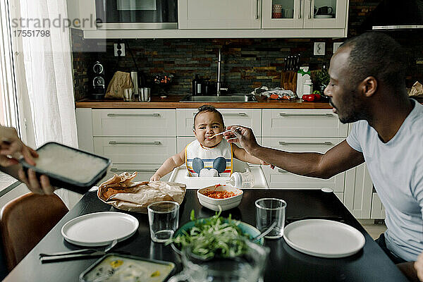 Vater füttert kleinen Jungen am Esstisch in der Küche