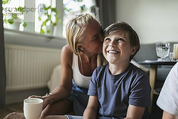 Mutter küsst lächelnden Sohn beim Fernsehen im Wohnzimmer