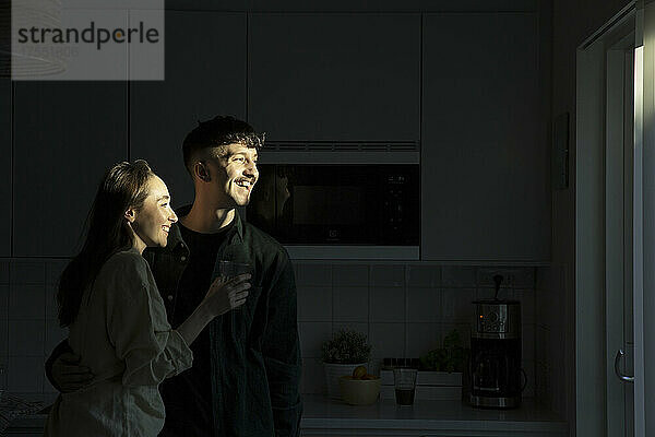 Glückliches junges Paar  das in der Küche steht und wegschaut