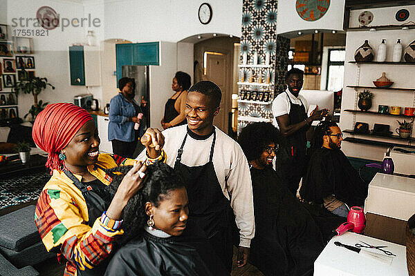 Lächelnde Friseurin im Gespräch mit einem männlichen Mitarbeiter  während sie einem Kunden im Friseursalon die Haare schneidet