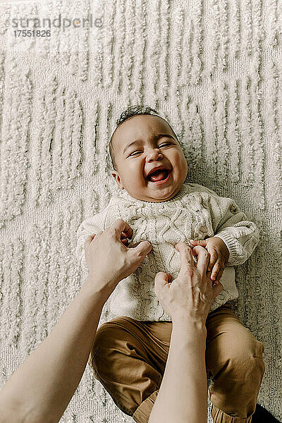 Abgeschnittenes Bild der Mutter kitzelt Baby auf der Decke liegend