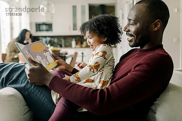 Glücklicher Vater liest mit seiner Tochter ein Buch im Wohnzimmer zu Hause