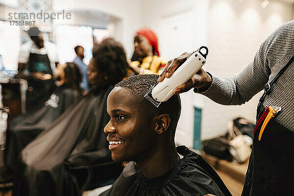 Mittelteil einer Friseurin beim Schneiden der Haare eines männlichen Kunden in einem Salon mit einem elektrischen Rasierapparat