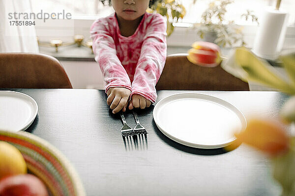 Mittelteil eines Mädchens mit Gabeln und Teller auf dem Tisch zu Hause