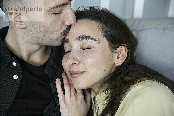 Zärtlicher Mann küsst die Stirn seiner Freundin im Schlafzimmer zu Hause