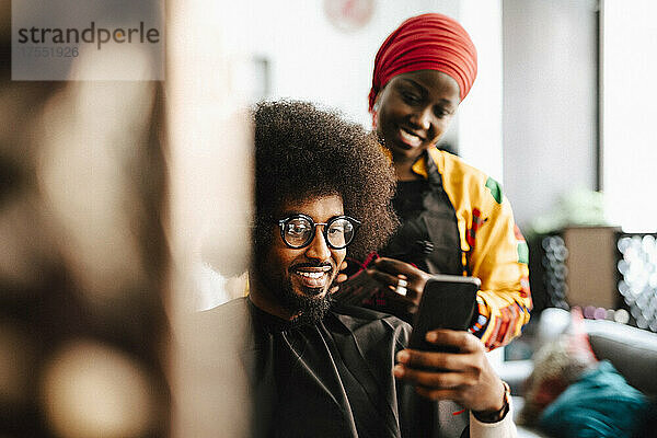 Lächelnder männlicher Kunde  der ein Selfie mit einer Friseurin im Friseursalon macht