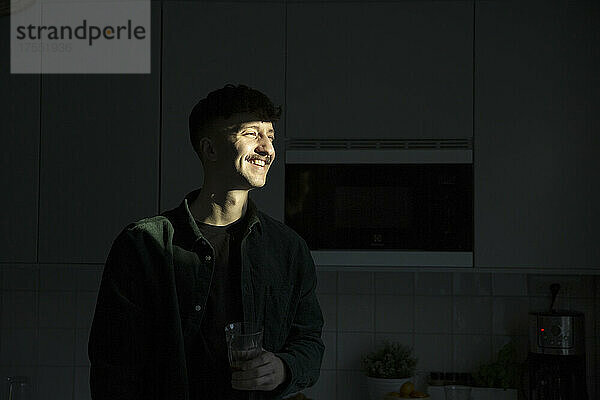 Lächelnder Mann mit Sonnenlicht im Gesicht in der Küche stehend