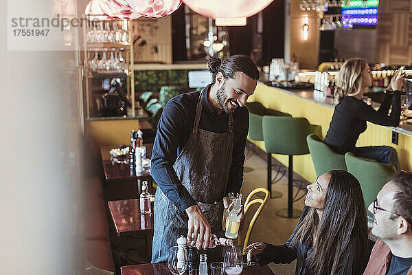 Lächelnder Kellner schenkt Wein an männliche und weibliche Kunden in einer Bar aus