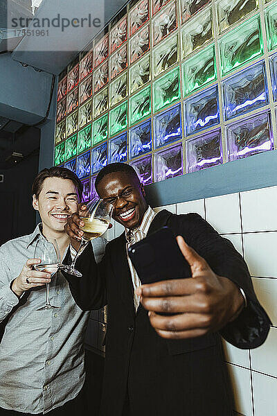 Fröhliche männliche Freunde mit Weingläsern machen ein Selfie mit ihrem Smartphone in einer Bar