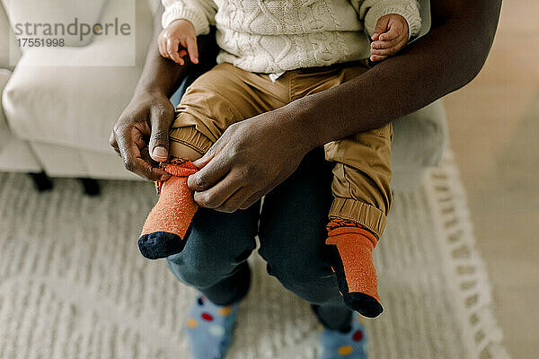 Hoher Blickwinkel des Vaters  der seinem Sohn im Wohnzimmer zu Hause Socken anzieht