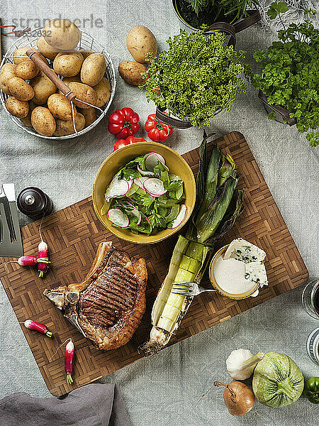 Gegrilltes Steak mit Salat  Lauch und Käsedip  Kartoffeln und Kräuter im Hintergrund