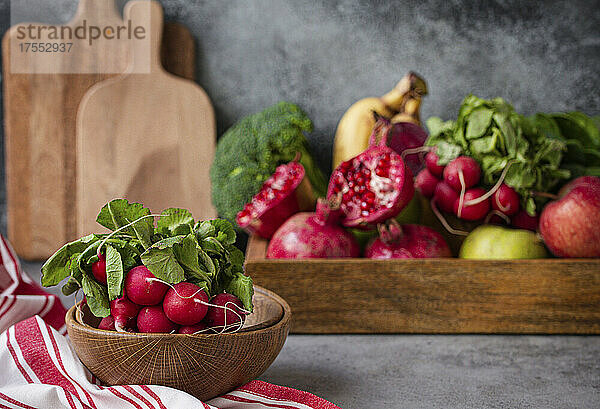 Ein Bund frisches Radieschen in Holzschale  frisches Obst und Gemüse dahinter
