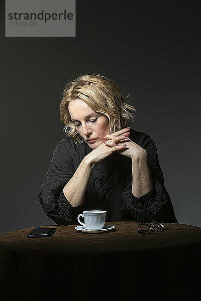 Blonde Frau mit Kaffee schaut auf ihr Smartphone