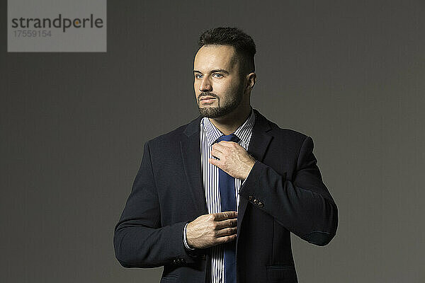 Porträt zuversichtlich  stilvoll Geschäftsmann im Anzug Anpassung Krawatte vor schwarzem Hintergrund