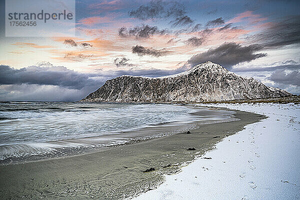 Wolken bei Sonnenuntergang über schneebedecktem Berggipfel und eisigem Skagsanden-Strand  Flakstad  Lofoten  Norwegen  Skandinavien  Europa