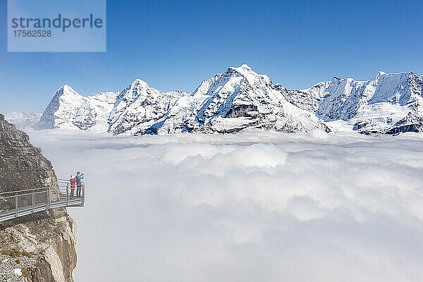 Zwei Personen fotografieren die schneebedeckten Gipfel von Eiger und Mönch im Nebel von einem erhöhten Steg aus  Murren Birg  Kanton Bern  Schweizer Alpen  Schweiz  Europa