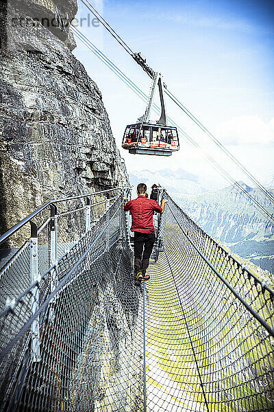 Eine Person betrachtet die Seilbahn vom Thrill Walk Felsenweg aus  Murren Birg  Jungfrau Region  Kanton Bern  Schweiz  Europa