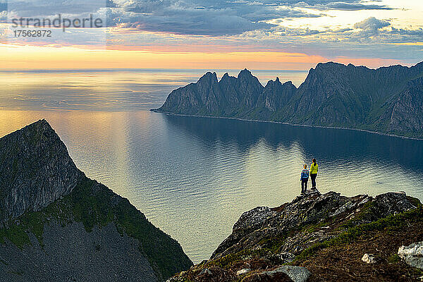 Zwei junge Frauen beobachten den Sonnenuntergang auf einem Berggipfel  Insel Senja  Provinz Troms  Norwegen  Skandinavien  Europa