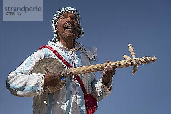 Marokkanischer Mann in traditioneller Kleidung spielt ein traditionelles Gimbri-Instrument  Ouarzazate  Atlasgebirge  Marokko  Nordafrika  Afrika