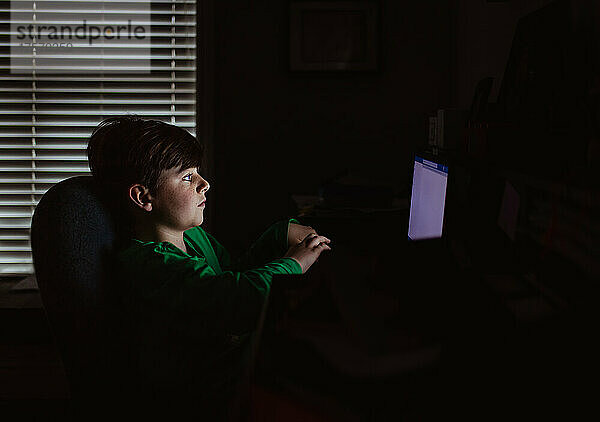 Kleiner Junge arbeitet an einem Laptop in einem dunklen Raum.