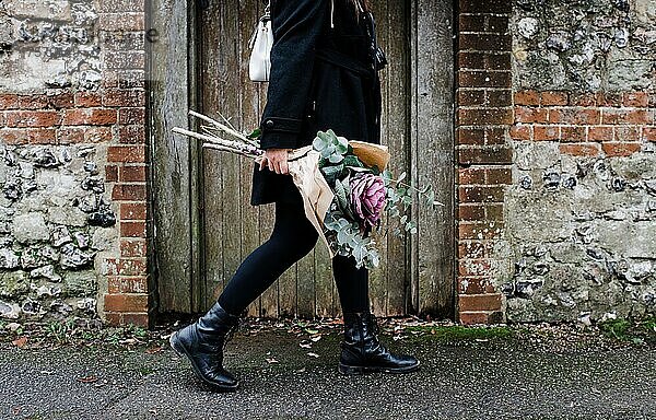 Frau geht mit Blumenstrauß durch gepflasterte Straßen