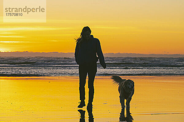 Hündin geht bei Sonnenuntergang mit ihrem Hund an der Küste Washingtons spazieren
