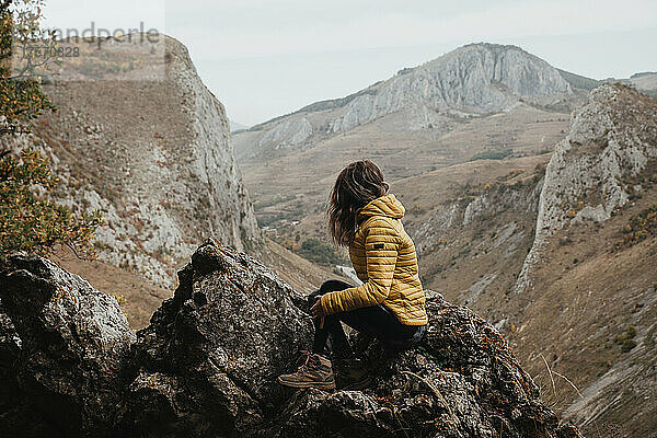 Mädchen mit gelber Jacke sitzt auf einer Klippe