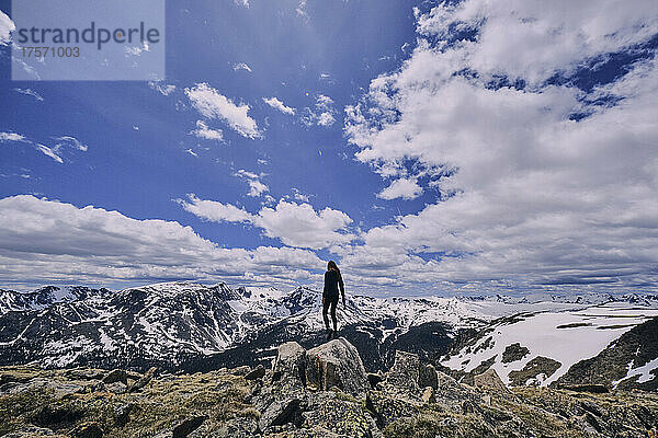 Junge Frau steht auf einem Felsen in einem Schneefeld in den Rocky Mountains