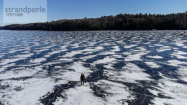 Luftaufnahme einer Person  die auf einem zugefrorenen  schneebedeckten See läuft.