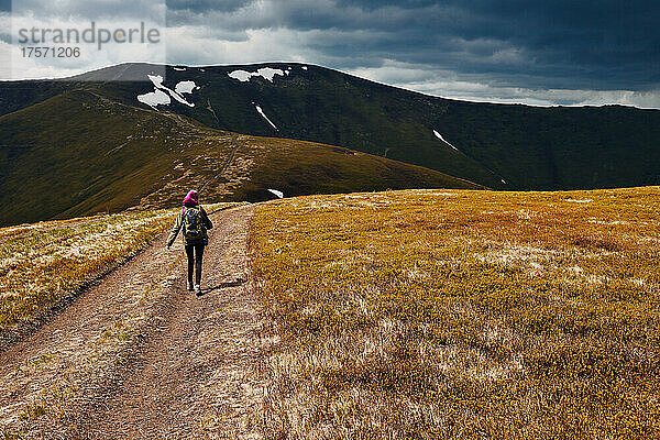 Eine Frau geht einen Bergpfad entlang einer Bergkette entlang.