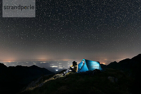 Ein Wanderer steht beim Zelten unter den Sternen und neben seinem Zelt